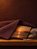 A folded plum linen cloth with one corner turned back, revealing printed photographs on an oak ledge in a lit arched niche.