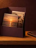 Printed photographs tucked into a plum card folder, a phone face-down beside it.