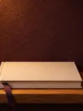 A closed cream linen photo album with a plum ribbon bookmark in a lit arched niche.