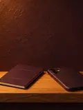 A closed plum passport and a phone lying face-down on an oak ledge in a lit arched niche.