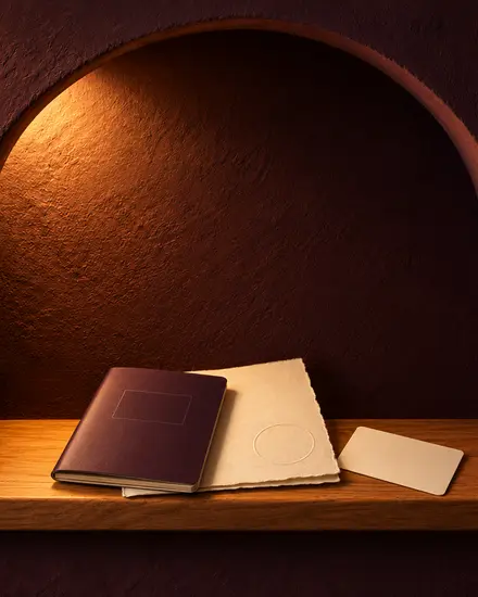 A closed plum passport on a cream certificate, with a card face-down, in a lit arched niche.